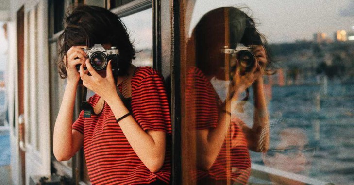 Žena drži foto-aparat i naslanja se na prozor