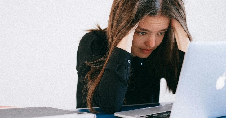 Devojka se drži za glavu dok gleda u laptop