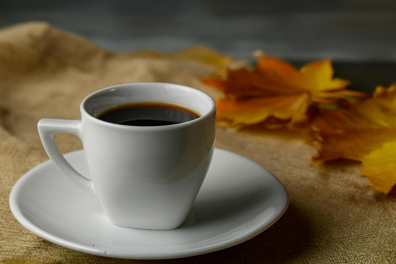 Bela &scaron;olja kafe na tanjiriću sa jesenjim žutim li&scaron;ćem u pozadini