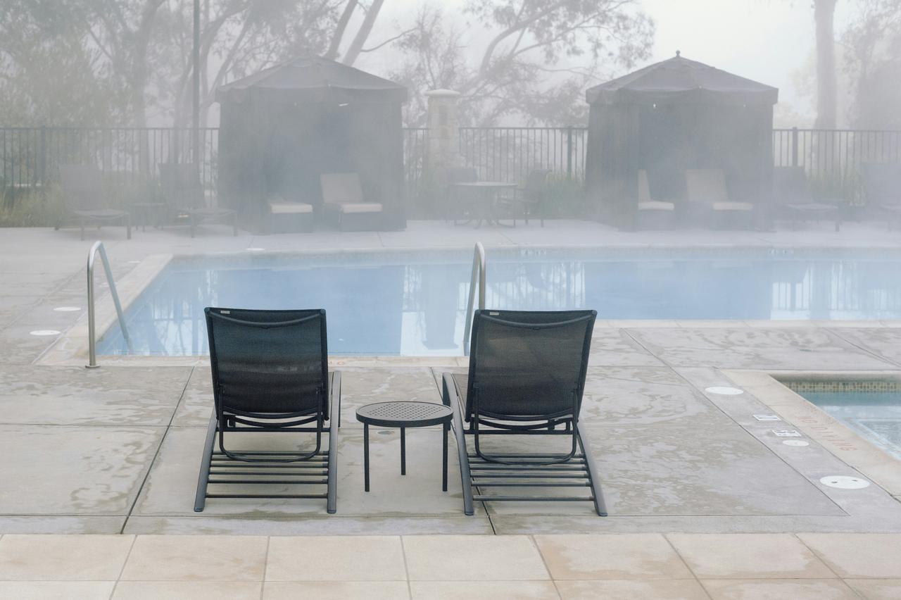 Dve ležaljke i mali okrugli stočić pored bazena okruženog maglom