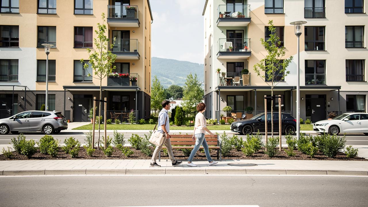 Dvoje ljudi hoda trotoarom ispred modernih stambenih zgrada