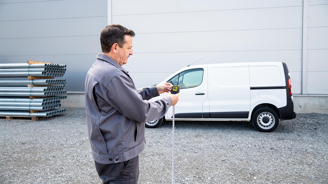 Mu&scaron;karac drži traku za merenje ispred belog kombija na industrijskom parkingu